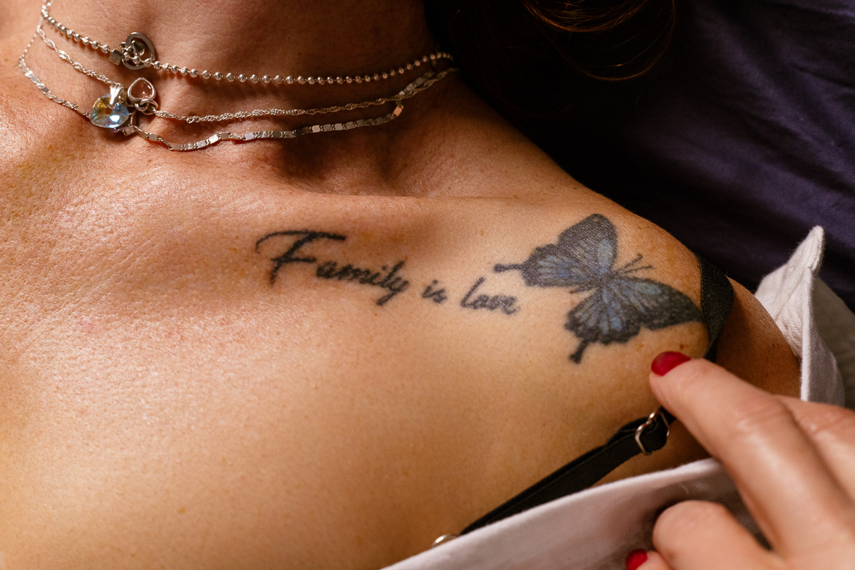 Detail image of tattoo on shoulder representing a blue butterfly and the phrase, Family is Love